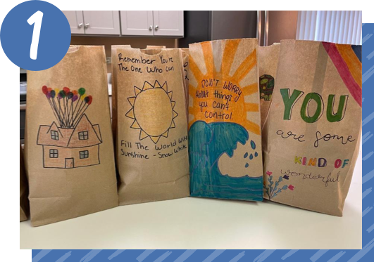 Paper lunch bags lined up on a counter are hand decorated with colorful pictures and encouraging messages.